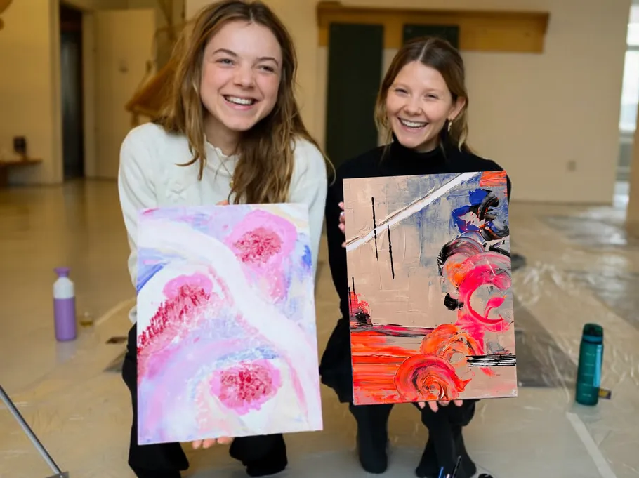 Zwei Frauen lachen, halten abstrakte Gemälde drinnen.