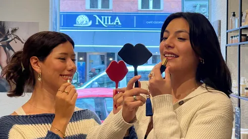 Two women apply lipstick using mirrors.