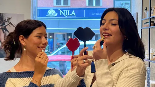 Two women apply lipstick using mirrors.