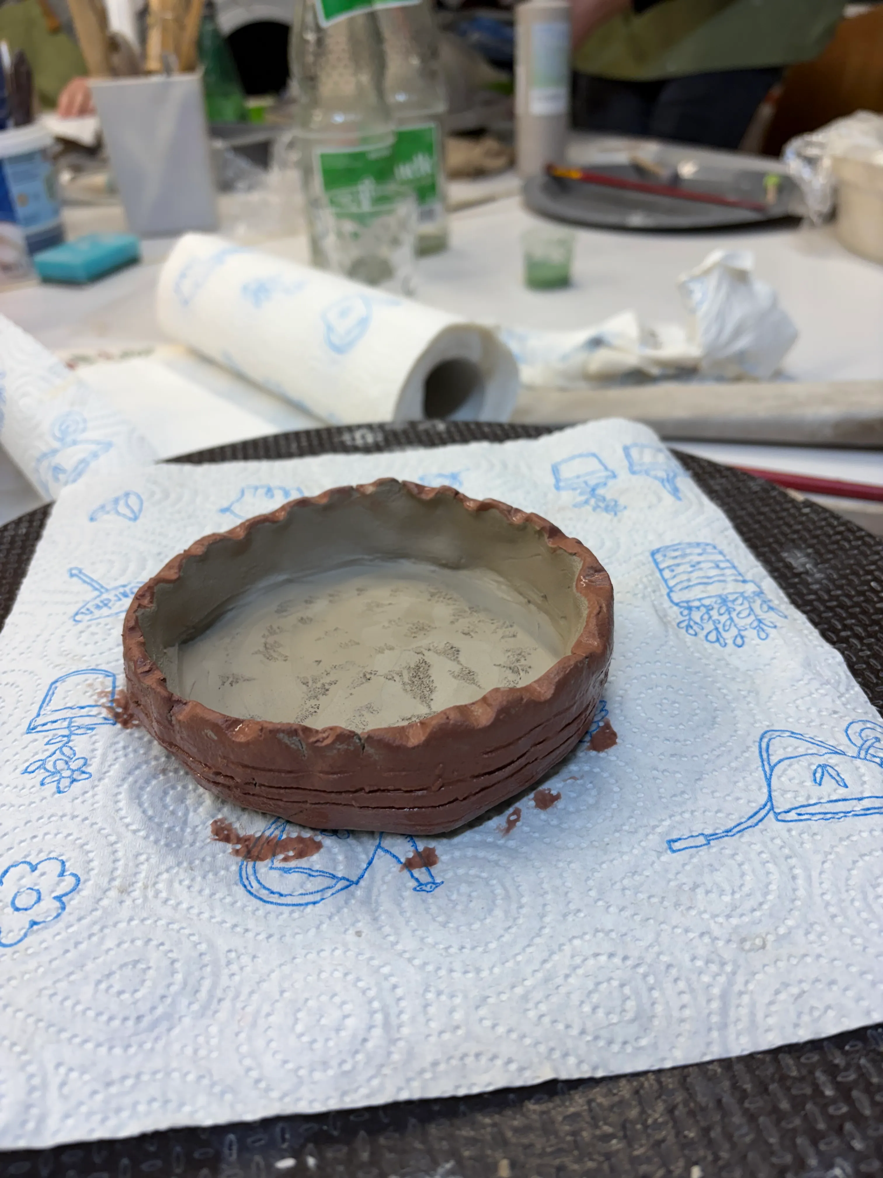 Clay bowl drying on paper towel, workshop table.