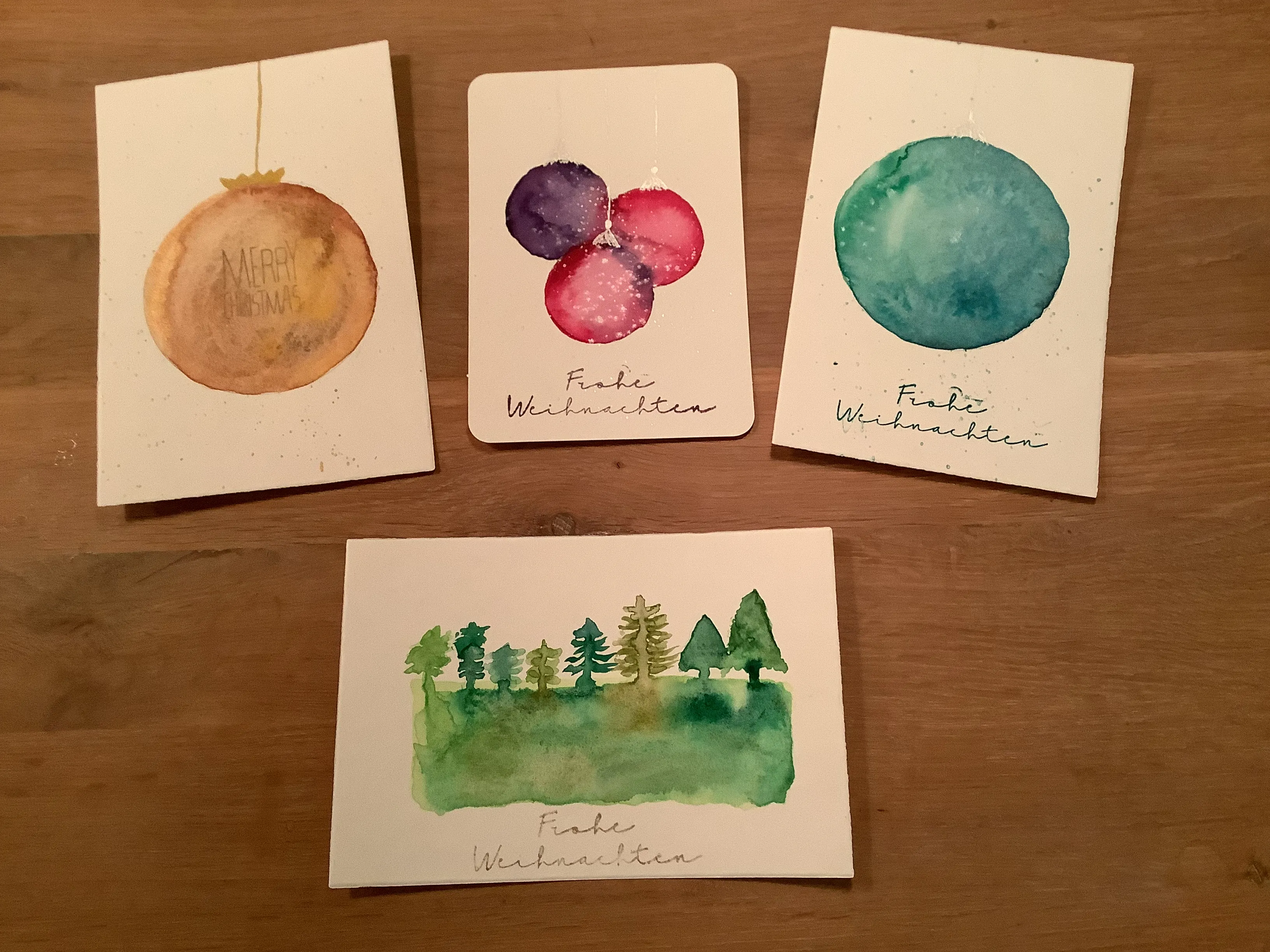 Vier Aquarell-Weihnachtskarten auf einem Tisch.
