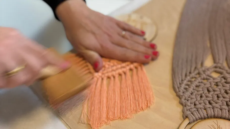 Hands brushing orange macramé on a table.