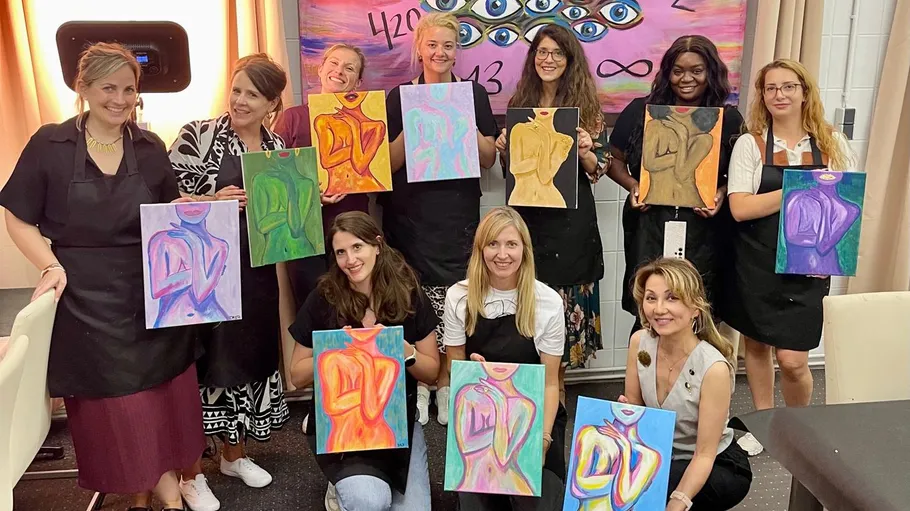 Group of women holding colorful paintings, indoor setting.