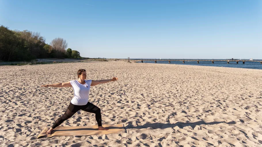 Person praktiziert Yoga am Sandstrand.