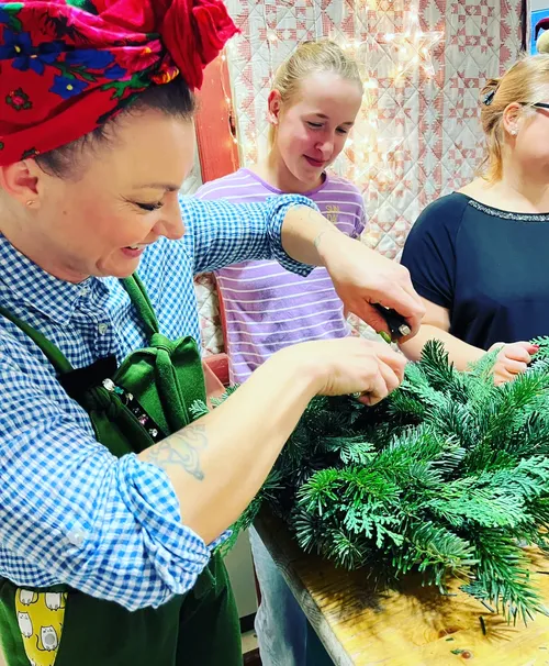 Women smiling, making wreath indoors.