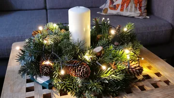 Kerze im dekorierten Kranz auf Holztisch.