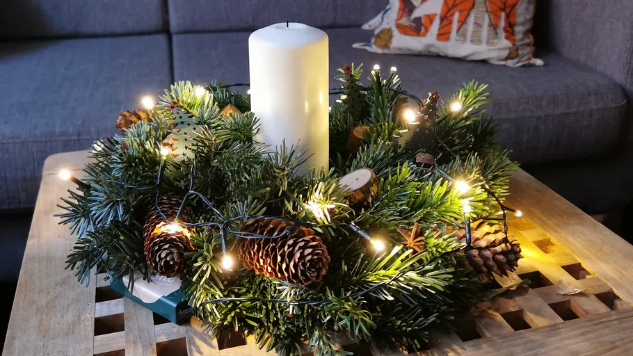 Candle in decorated wreath on wooden table.