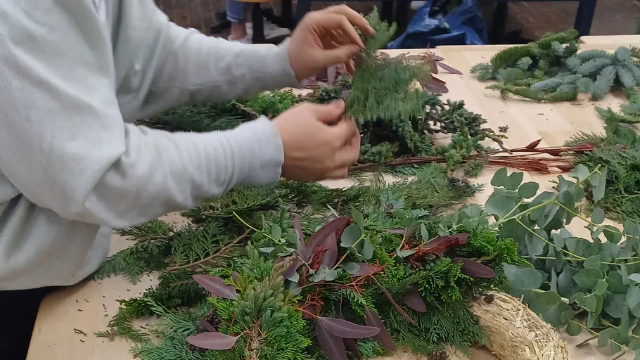 Person arranging greenery on wooden table.
