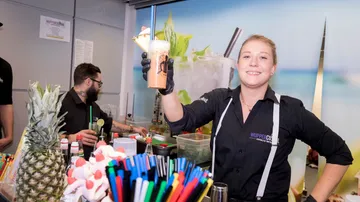 Barkeeper serviert Getränk in belebter Bar.