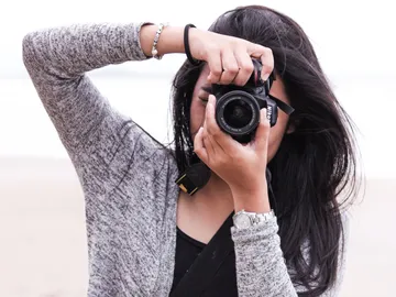 Eine Person fotografiert am Strand mit einer Kamera.