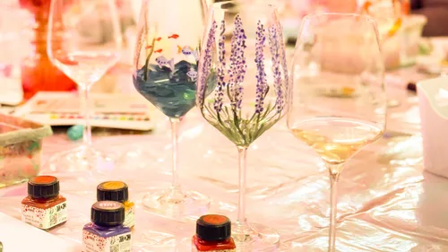 Bemalte Weingläser mit Farbflaschen auf Tisch.