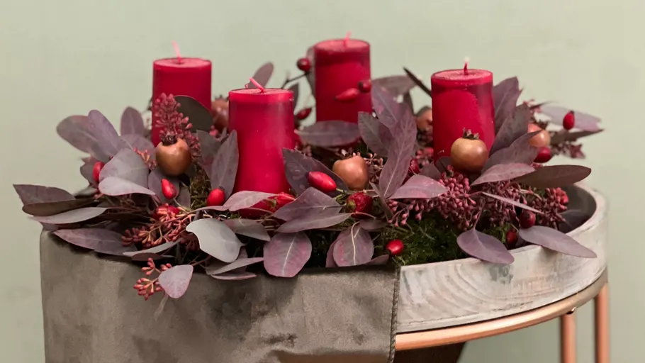 Four red candles with festive decorations on table.