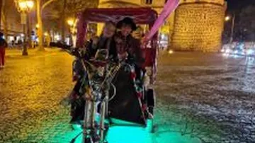 Bicycle rickshaw at night, colorful lights surround.