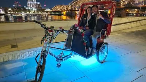 Paar sitzt in Rikscha bei beleuchteter Brücke.