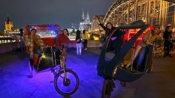 People on rickshaws at night near bridge.