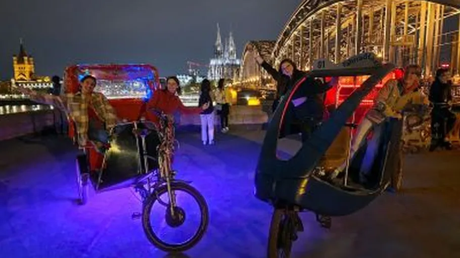 People on rickshaws at night near bridge.
