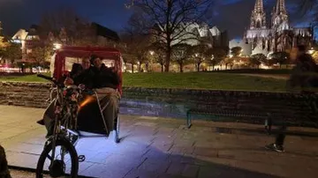 Bicycle taxi with passengers near illuminated cathedral.