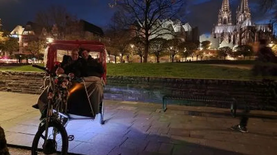 Bicycle taxi with passengers near illuminated cathedral.