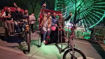 People on rickshaws, night, Ferris wheel background.