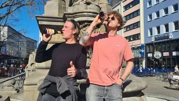 Two men drink beer in sunny urban area.