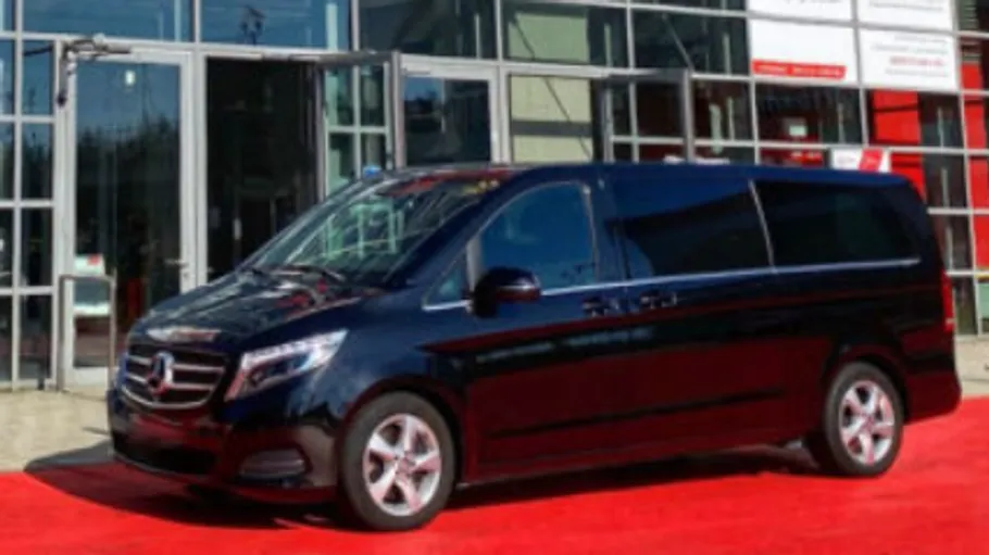 Black van parked on red carpet outside building.