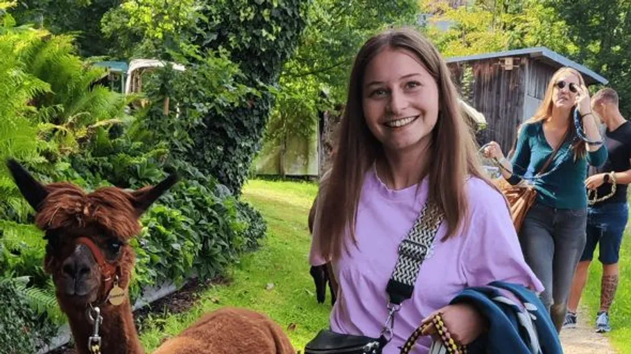 Frau lächelt mit Alpaka, draußen in Grün.