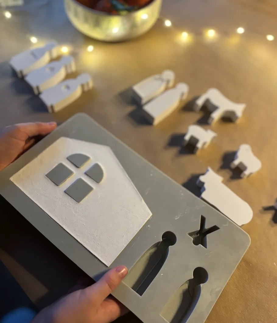 Hands holding clay mold with nativity shapes.