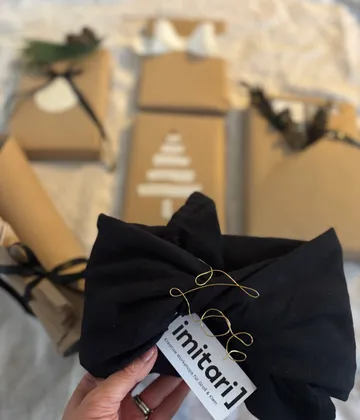 Hand hält verpacktes Geschenk mit anderen Geschenken dahinter.