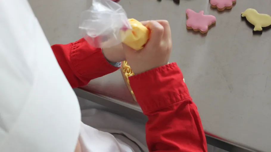 Child decorates cookies with icing on table.