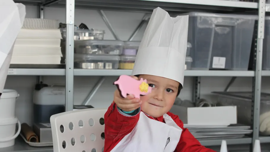 Child in chef attire holding pink object.