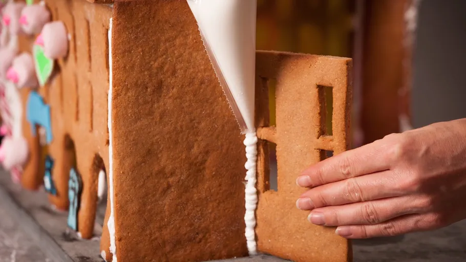Person assembling a gingerbread house piece.