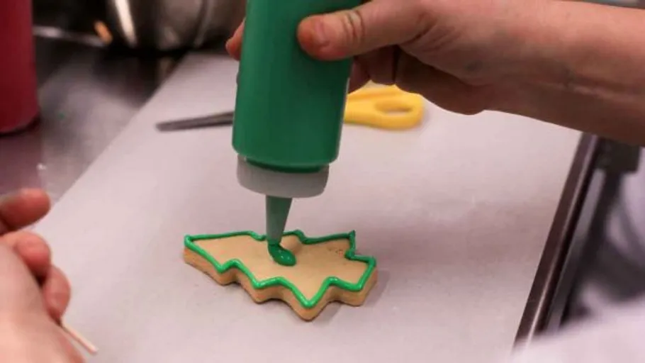 Person decorating cookie with green icing.
