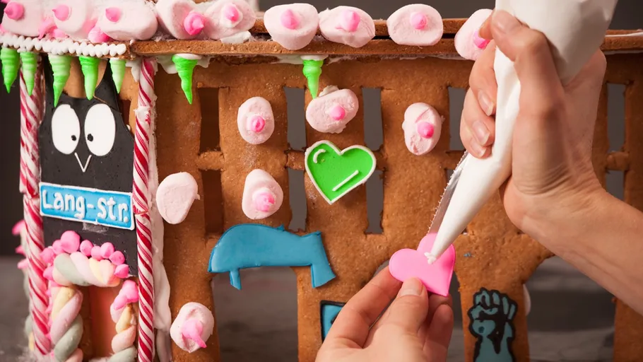 Hände verzieren Lebkuchenhaus mit Zuckerguss.