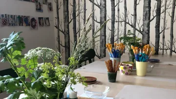 Art supplies on table, forest-themed wallpaper.