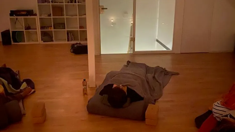 Person auf Yoga-Matte in dunklem Raum ruhend.