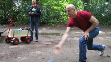 Mann spielt draußen Kegeln, Freund schaut zu.