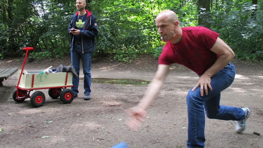 Mann spielt draußen Kegeln, Freund schaut zu.