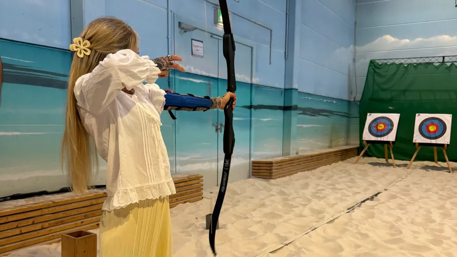 Woman aiming bow at indoor archery range.