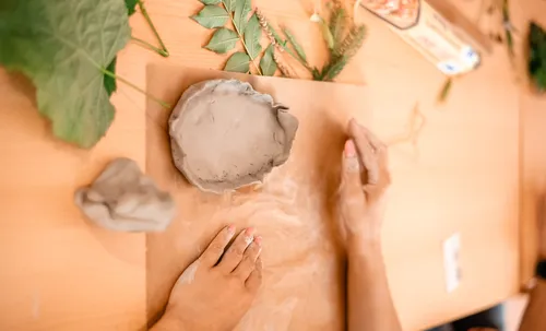 Hands shaping clay with leaves nearby.
