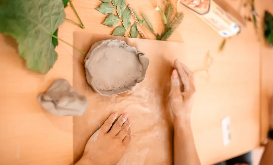 Hands shaping clay with leaves nearby.