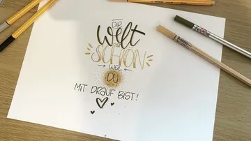 Handschriftlicher Spruch mit Stiften auf Tisch.