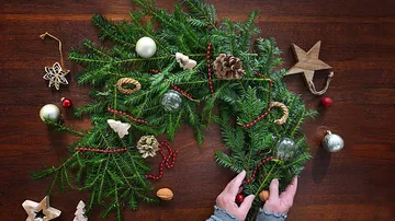 Hands arranging Christmas wreath on wooden table.