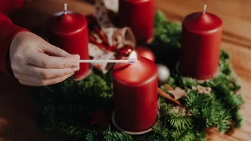 Hand zündet rote Kerze am Adventskranz an.