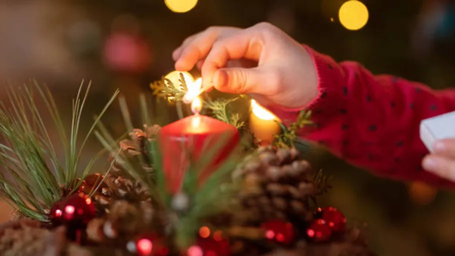 Hand lighting red candle on festive wreath.