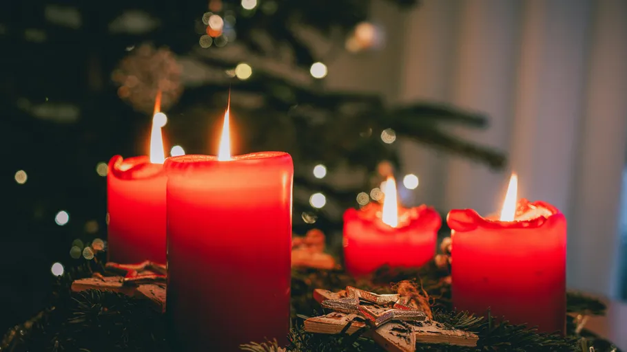 Red candles glowing on Christmas wreath indoors.