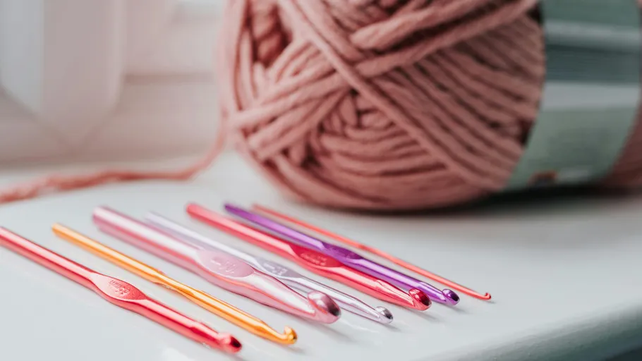 Colorful crochet hooks beside pink yarn.