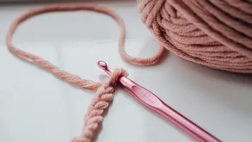 Crochet hook with pink yarn on table.