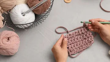 Hände häkeln mit Garn auf einem Tisch.