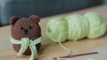 Gehäkelter Bär und Garn auf Holztisch.