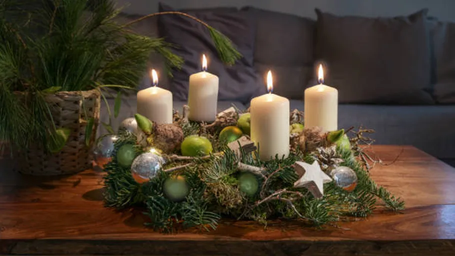 Adventskranz mit vier brennenden Kerzen auf Tisch.